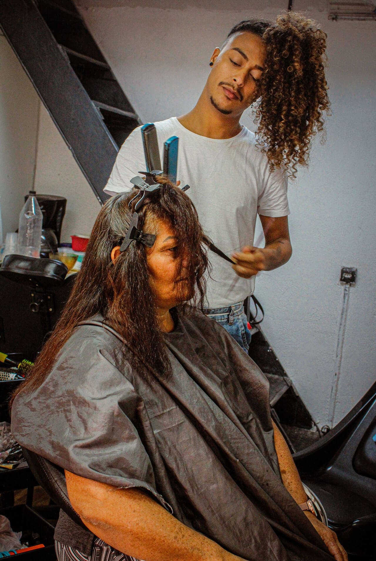 A imagem retrata um cabeleireiro em um salão de beleza do aglomerado fazendo um corte em uma cliente.