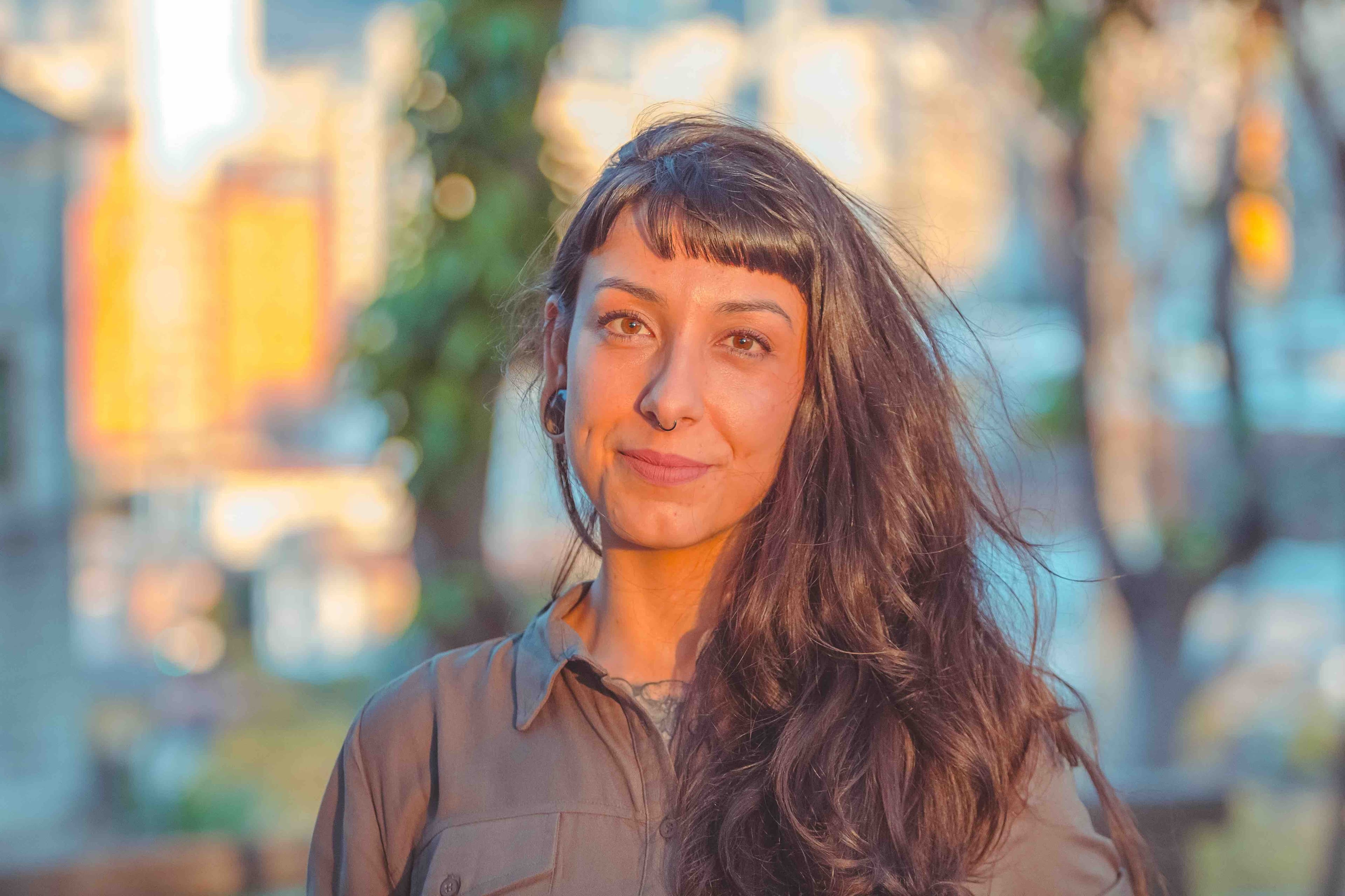 A foto mostra Jéssica, uma mulher branca de cabelos lisos, escuros, de lado, franja e um sorriso tímido. Ao fundo, paisagem de cidade.
