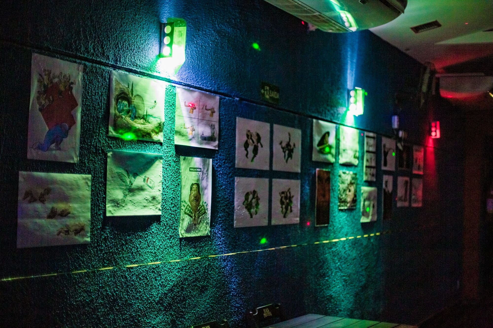 A foto mostra uma parede interna da casa matriz. A parede é azul e nela estão coladas diversas artes impressas em papel a4.