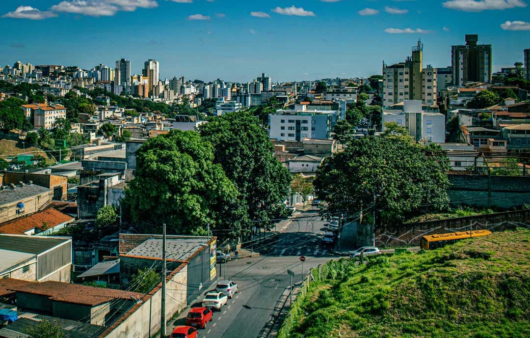 A foto traz uma imagem mais abrangente do bairro Jardim América e da sua região. No centro um cruzamento entre ruas, bastante arborizado, e ao redor e até o fundo da imagem diversos prédios de diferentes tamanhos. No canto direito da foto parte do terreno destinado ao Parque Jardim América.
